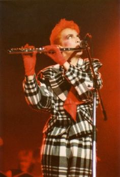 a woman with red hair holding a flute in front of her face while standing on stage