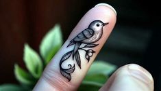 a person's finger with a bird tattoo on it and a plant in the background