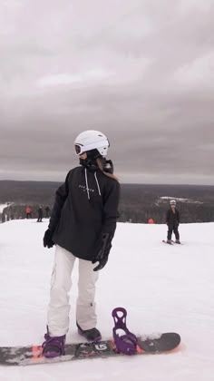 a snowboarder is standing on the top of a snowy hill with other skiers in the background