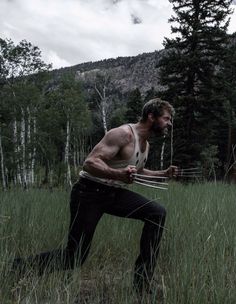 a man in black pants and white tank top holding a pair of scissors while standing in tall grass