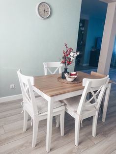 a dining table with white chairs and a clock on the wall