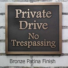 a sign that reads private drive no trespassing bronze lettering on a brick wall