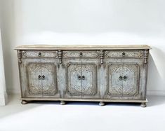 an old white painted sideboard with ornate carvings on the doors and drawers, against a plain white wall