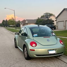 a green beetle parked on the side of a road next to houses and trees in front of a street light