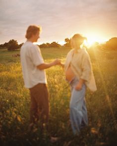 two people standing in a field with the sun setting behind them and one person holding his hand out