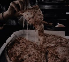 a person taking a slice of pizza out of a box with melted cheese on it