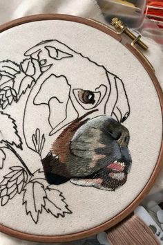 an embroidery project with a dog's face and leaves on the hoop hanging in front of it