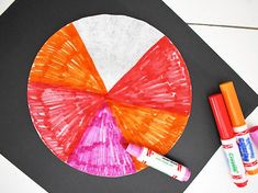 some crayon markers are next to a paper plate with a colorful wheel on it