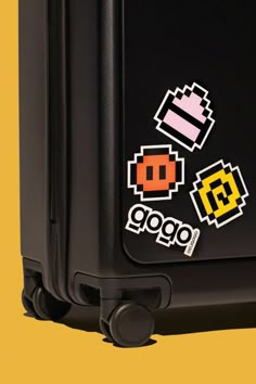 a piece of black luggage with stickers on the handles and sides, sitting against a yellow background