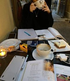 a woman sitting at a table holding a coffee cup in front of her face and looking into the camera