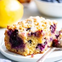 blueberry crumb muffins on a plate with a fork and bowl of fruit in the background