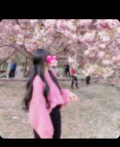 a woman with long black hair wearing a pink sweater and holding a flower in her hand