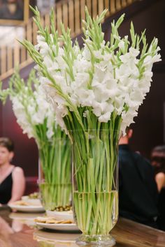 some white flowers are in a glass vase on a table with other plates and food