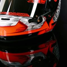 an orange motorcycle helmet on display in a dark room with reflective glass and black background