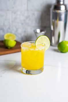 a glass filled with orange juice next to limes and a shaker on a counter