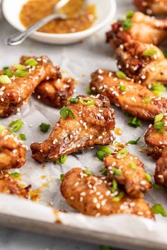 chicken wings with sesame seeds and green onions on a sheet of parchment paper next to dipping sauce