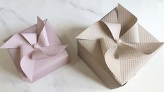 two origami boxes sitting next to each other on a white counter top, one is pink and the other is beige