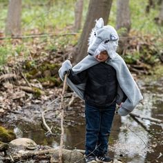 a young boy wearing a wolf mask and carrying a stick across a stream in the woods