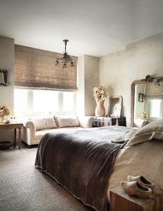 a bedroom with a large bed, mirror and couch in front of two windows that have roman shades on them