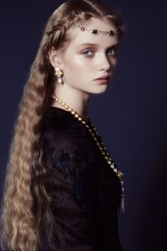 a woman with long blonde hair wearing a black dress and gold jewelry on her head