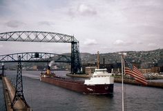 a large boat traveling down a river next to a bridge and an american flag on the side