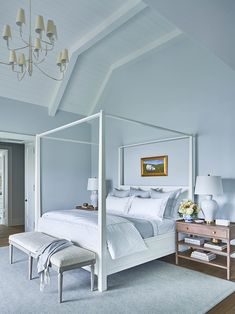 a white canopy bed sitting in a bedroom next to a wooden dresser and lamp on top of a hard wood floor