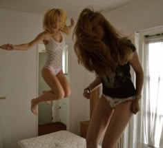 two women jumping in the air on top of a bed