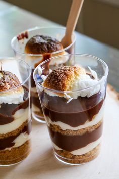 three desserts with chocolate sauce and whipped cream in small cups on a wooden tray