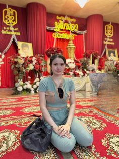 a woman sitting on the floor in front of a stage with red curtains and decorations