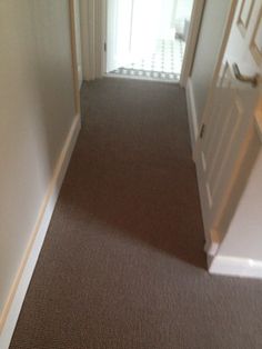 an empty hallway leading to a door and another room in the house with carpeting