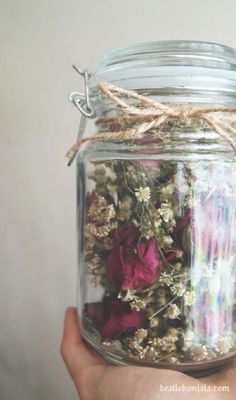 a hand holding a jar filled with dried flowers