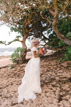 a woman standing on top of a sandy beach holding a bouquet of flowers in her hand