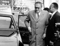 two men walking down the street with cars behind them and buildings in the back ground