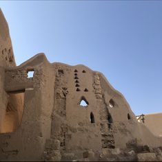 an old adobe building with holes in the side and sky behind it, on a sunny day