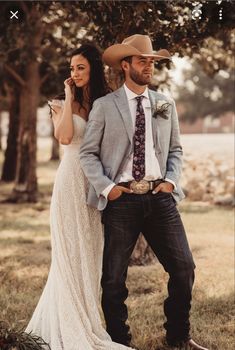 a man and woman standing next to each other in front of trees wearing cowboy hats