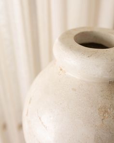 a large white vase sitting on top of a table next to a curtained window