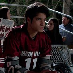 a young man sitting on the bench in front of some people holding signs and wearing hockey gloves