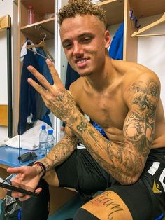 a man with tattoos sitting in front of a mirror holding his hand up to the camera