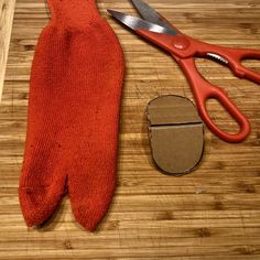 a pair of red gloves sitting next to a pair of scissors on top of a wooden table