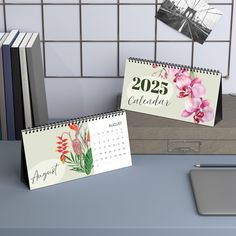 two calendars sitting on top of a desk next to books and a laptop computer