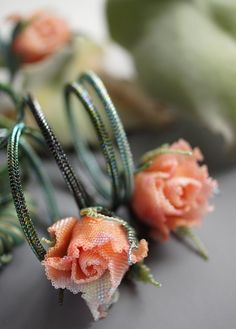 two roses are sitting next to each other on a gray surface with green stems and beads