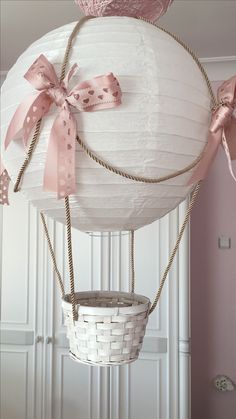 a white basket hanging from the ceiling with pink bows and ribbons on it's sides