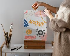 a woman is painting on an easel next to some paintbrushes and other art supplies