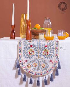 an embroidered table cloth with candles and fruit on it