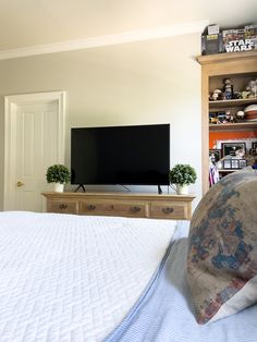 a bedroom with a large flat screen tv on top of a wooden entertainment center next to a bed