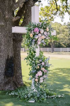 a cross decorated with flowers and greenery next to a tree