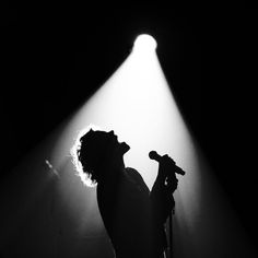 a person holding a microphone in front of a spotlight on a dark stage with light coming from behind