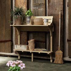 a wooden shelf with flowers and brooms on it next to a potted plant