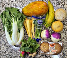 an assortment of fruits and vegetables sitting on a counter top with eggs, potatoes, spinach, carrots, squash, onions, broccoli, radishes