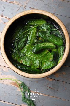 a wooden bowl filled with green vegetables on top of a wooden table next to a leafy plant